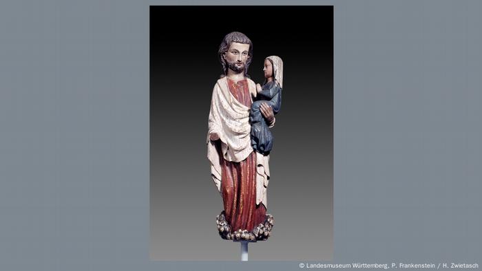 Eine mittelalterliche Holzskulptur zeigt Christus, der die Seele seiner Mutter Maria in Form eines Kindes auf dem Arm trägt.