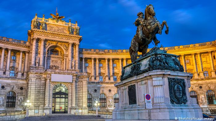 A large statue of a prince riding a horse in front of the Hofburg Palace lit up at night.