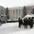Foto mostra um veículo militar e homens de uniforme policial em frente a um prédio. Está nevando. 