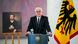 Frank-Walter Steinmeier, man standing at lectern next to a German Federal eagle flag , painting on easel in the baclground Frank-Walter Steinmeier, man standing at lectern next to a German Federal eagle flag , painting on easel in the baclground