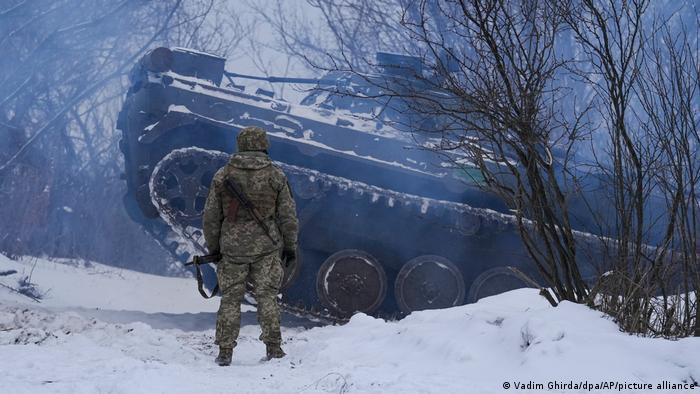 A Ukrainian soldier stands in front of a tank at a Luhansk frontline covered in snow