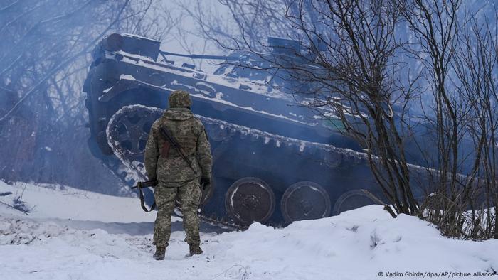 A Ukrainian soldier stands in front of a tank at a Luhansk frontline covered in snow