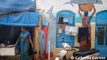 A women buys fish from a stall in Versova koliwada, next to a Bombay61 mural which depicts the historical importance of the area as a fish trading market.