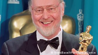 John Williams hält die Oscar-Trophäe in den Händen und lächelt.