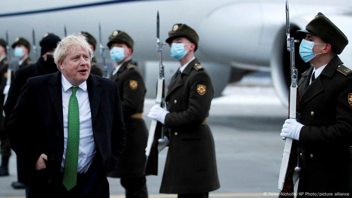 British prime minister Boris Johnson, in a black suit and green tie, walks past masked soldiers on the airport tarmac after arriving for talks in Kyiv