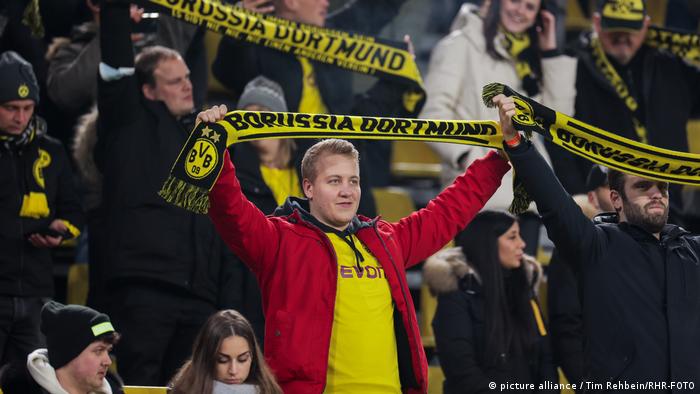 Fan von Borussia Dortmund hält auf der Tribüne seinen Fanschal in die Höhe