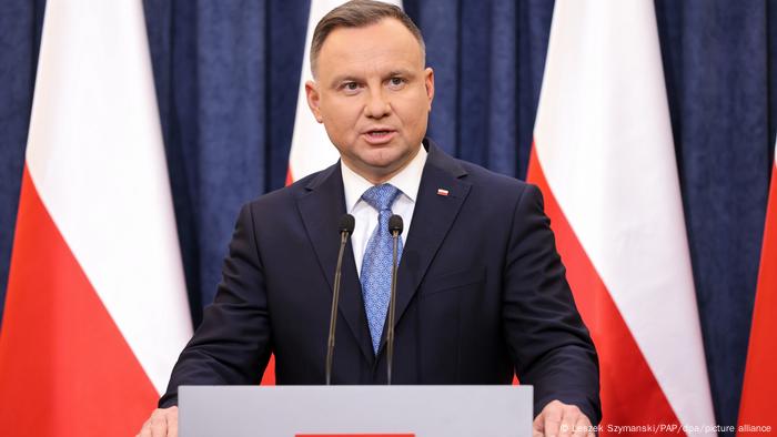 Polish president Andrzej Duda in front of red and white Polish flags against a blue background