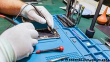 Technician examining damaged mobile phone at workbench at repair shop model released Symbolfoto property released LJF01840 
