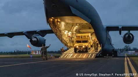 Veículo militar é retirado de dentro de avião em um aeroporto. 