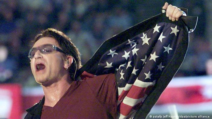 U2-Sänger Bono beim Super Bowl mit einer Jacke, deren Innenfutter aus dem Muster der amerikanischen Flagge besteht.
