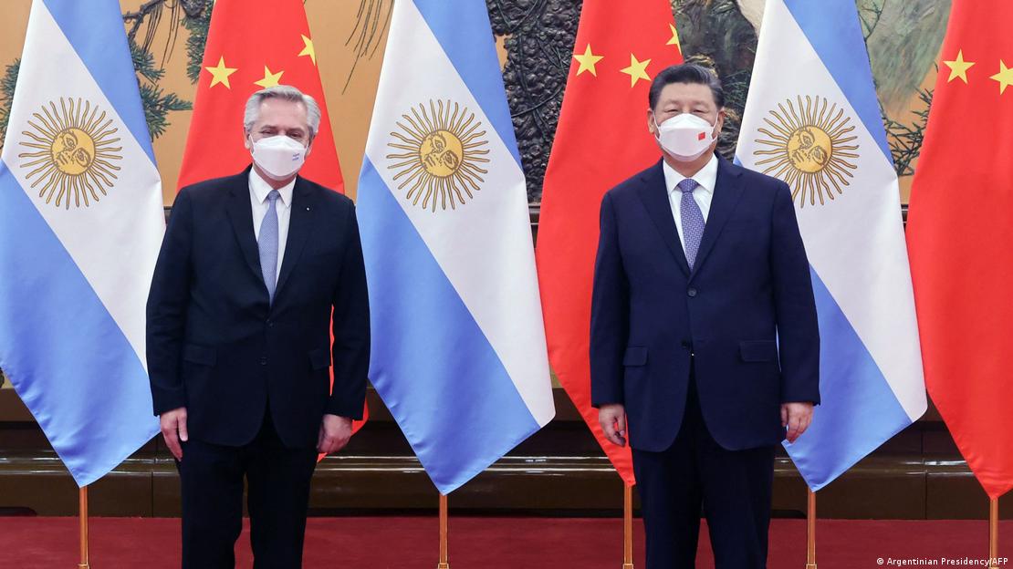 A foto mostra os presidentes da Argentina, Alberto Fernández, e da China, Xi Jinping. Ambos vestem ternos escuros, camisas brancas e gravatas azul-claro, e posam para fotos em frente a bandeiras argentinas e chinesas intercaladas.