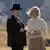Filmstil aus "The Power of the Dog": Ein Mann mit Hut und Mantel und eine Frau mit Pullover und Rock stehen mit Teetassen im Freien