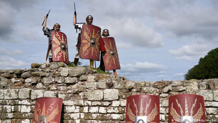 Actors dressed up as Roman soldiers holding spears and shields stand on Hadrian's Wall.