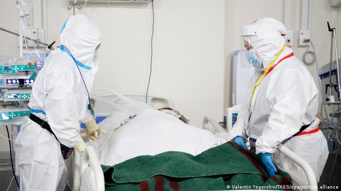 Zwei Personen in Schutzkleidung stehen an dem Bett eines Corona-Patienten in Russland