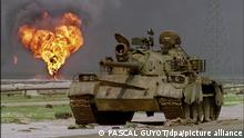 ARCHIV - Das Wrack eines verlassenen irakischen Panzers vom Typ T-62 sowjetischer Bauart steht am 02.04.1991 am Rande einer Wüstenstraße in Kuwait während im Hintergrund ein brennendes Bohrloch des Al-Ahmadi Ölfeldes zu sehen ist (Archivfoto). Vor 20 Jahren begann in der Nacht zum 17. Januar 1991 der Golfkrieg zur Befreiung Kuwaits. Der irakische Diktator Saddam Hussein hatte das von ihm angedrohte «brennende Kuwait» wahr gemacht und ließ mehr als 700 Ölquellen anzünden. Die letzte wurde erst knapp zehn Monate später am 6. November gelöscht. Foto: Pascal Guyot AFP/dpa (zu dpa Themenpaket zum 20. Jahrestag des Golfkriegs zur Befreiung Kuwaits (Beginn in der Nacht zum 17. Januar 1991) +++ dpa-Bildfunk +++