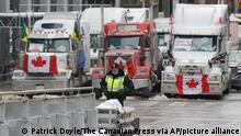 A police officer stands in front of trucks blocking downtown streets as a rally against COVID-19 restrictions, which began as a cross-country convoy protesting a federal vaccine mandate for truckers, continues in Ottawa on Wednesday, Feb. 9, 2022. (Patrick Doyle/The Canadian Press via AP)