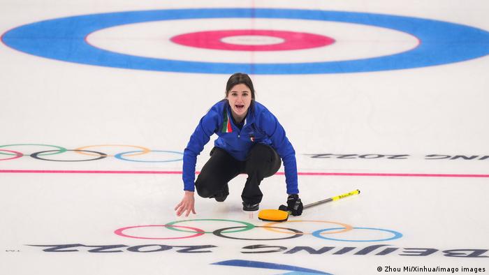 Stefania Constantini kneels on the curling rink at the Winter Olympics