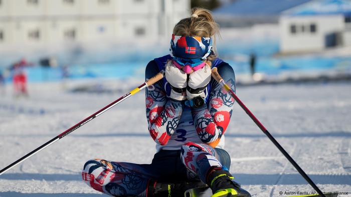 Therese Johaug, her head in her hands while sitting on the ski slope at the Winter Olympics