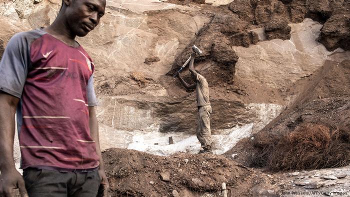 Ein Mann schwingt einen großen Vorschlaghammer hoch über den Kopf, mit dem er am Grund der Mine Granitblocken zerschlägt.