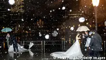 TOPSHOT - Couples prepare for their wedding photo shooting in front of Tokyo Station as it snows in Tokyo on February 10, 2022. (Photo by Philip FONG / AFP) (Photo by PHILIP FONG/AFP via Getty Images)