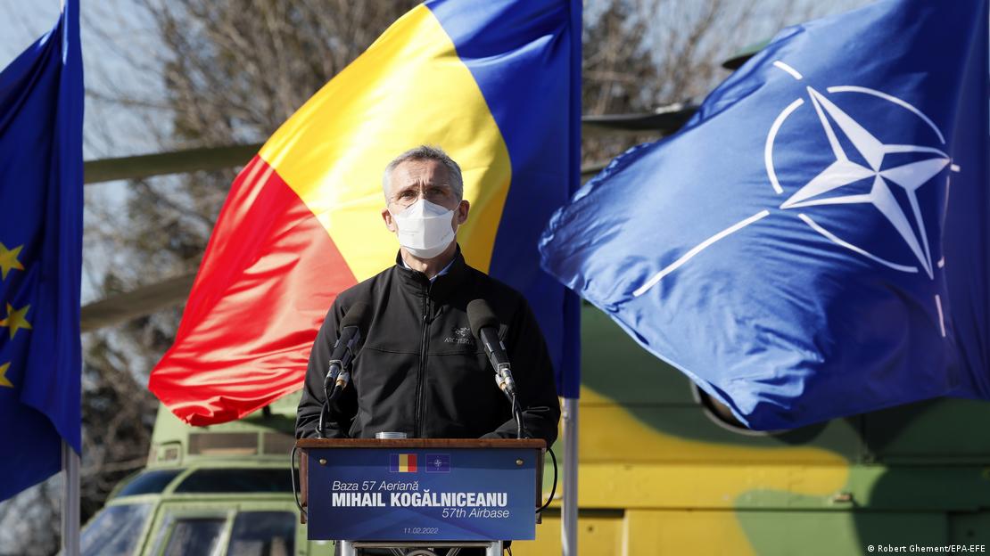 Jens Stoltenberg standing at a podium in front of a microphone. Behind him are the Romanian, NATO and EU flags.
