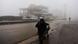A man pulls a cart in the haze on the outskirts of Sweida, Syria. Cars and the skeleton of a building can be seen in the background. A man pulls a cart in the haze on the outskirts of Sweida, Syria. Cars and the skeleton of a building can be seen in the background.