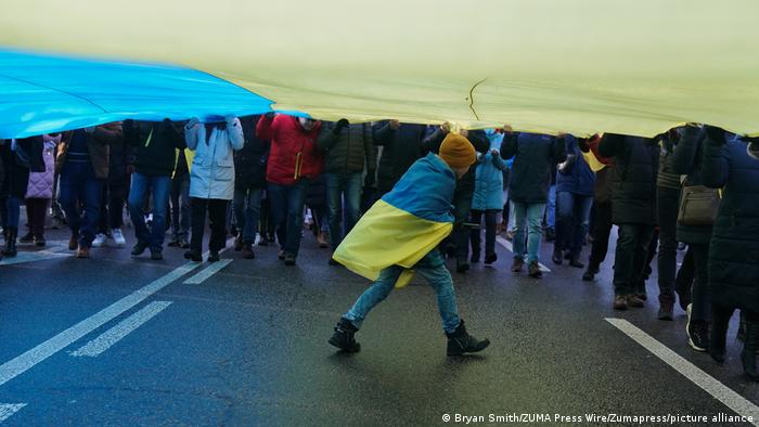 A child wearing a Ukrainian flag walks underneath a larger Ukrainian flag in Kyiv