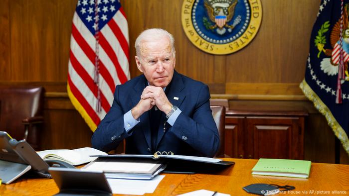 Joe Biden sits at a desk with a binder open in front of him, the presidential seal behind