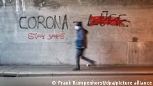 Ein Mann mit Mund-Nasen-Schutz geht durch eine Offenbacher Eisenbahnunterführung, an deren Wand «Corona Lüge» geschrieben steht, wobei mit roter Farbe das gesprühte Wort «Lüge» (r) durchgestrichen wurde. Stattdessen wurde «Stay Safe» (Bleibe sicher) unter das Wort «Corona» gesprüht. (zu dpa: «Selbsthilfegruppe für Angehörige von Verschwörungsanhängern startet») +++ dpa-Bildfunk +++