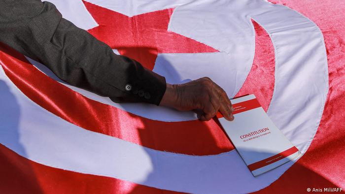 متظاهر في تونس يضع نسخة من دستور 2014 على العلم التونسي إحتجاجا على خطوات الرئيس سعيّد