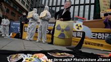 Environmental activists wearing a mask of Japanese Prime Minister Yoshihide Suga and protective suits perform to denounce the Japanese government's decision on Fukushima water, near the Japanese embassy in Seoul, South Korea, Tuesday, April 13, 2021. Japan's government decided Tuesday to start releasing massive amounts of treated radioactive water from the wrecked Fukushima nuclear plant into the Pacific Ocean in two years - an option fiercely opposed by local fishermen and residents. (AP Photo/Lee Jin-man)