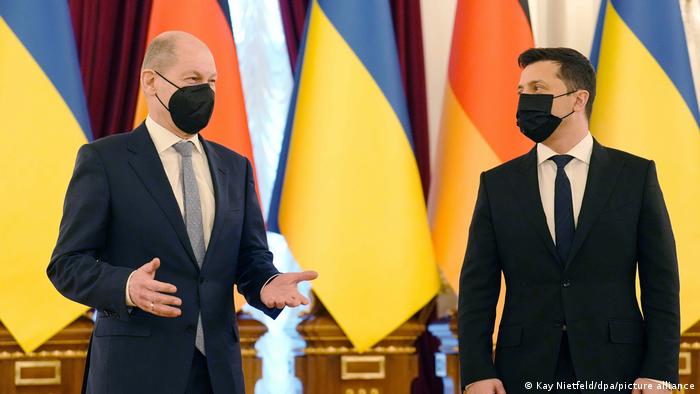 Scholz (left) and Zelenskyy stand in front of flags, wearing black face masks