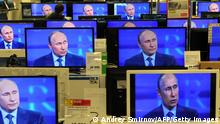 A customer walks past the TV screens in a shop in Moscow, on April 25, 2013, during the broadcast of President Vladimir Putin's televised question and answer session with the nation. AFP PHOTO / ANDREY SMIRNOV (Photo credit should read ANDREY SMIRNOV/AFP via Getty Images)
