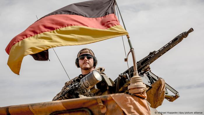 A German soldier in Mali is seen next to a machine gun and in fromt of a German flag