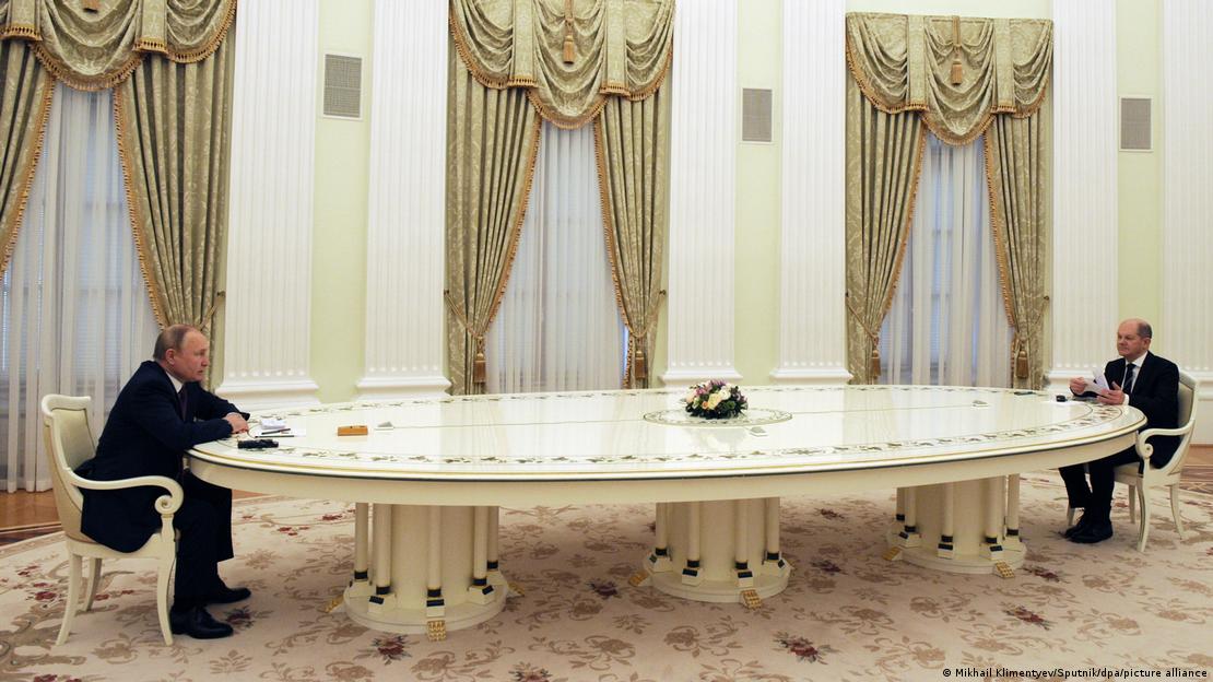 Chanceler federal alemão, Olaf Scholz, e presidente russo, Vladimir Putin, sentando a uma longa mesa branca