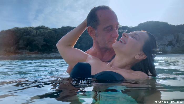 Film still from 'Both Sides of the Blade': A woman smiles as she is embraced by a man in the water.