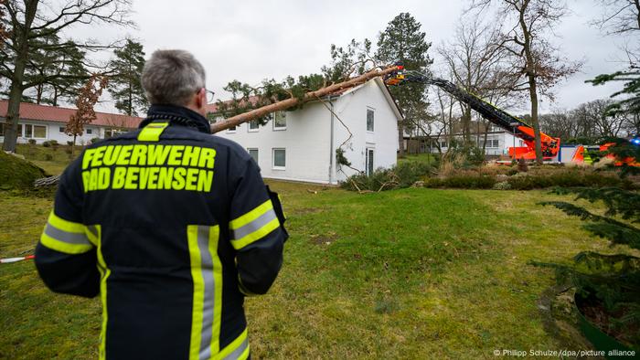 Un bombero de pie junto a una casa golpeada por un árbol