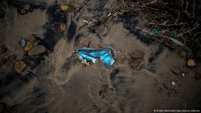 A disposable mask lies on a beach 