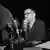 Black and white photo of Bertolt Brecht sitting in front of microphones