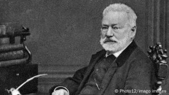 Eine Schwarz-Weiß-Fotografie von 1872 des sitzenden Schriftstellers Victor Hugo, im Hintergrund ein Bücherstapel