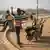 Two young men leaning on wheelbarrows by a roadside and a youth with carrying a package on his shoulders