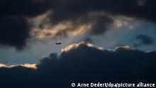17.02.2022, Hessen, Frankfurt/Main: Während die Sonne hinter dunklen Wolken verdeckt ist, befindet sich ein Flugzeug im Landeanflug auf den Frankfurter Flughafen. Foto: Arne Dedert/dpa +++ dpa-Bildfunk +++