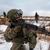 Soldier in winter uniform aiming a rifle on a bare, partially snowy moorland