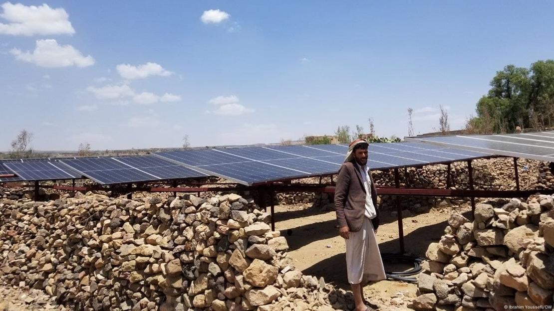 A farmer stands in front of solar panels in Yemen. 