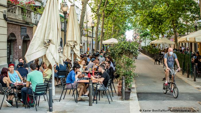 Barcelona. Die Straße ist für den Autoverkehr gesperrt. Die Bürger sitzen draußen in Cafés und ein Fahrradfahrer fährt vorbei.