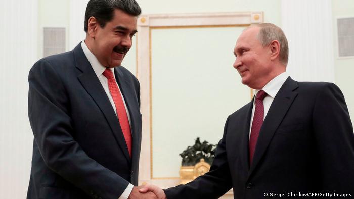 Nicolas Maduro (left) shaking hands with Vladimir Putin. Both are wearing dark suits and red ties.