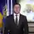Ukrainian president Volodymyr Zelenskyy in a black suit and tie; blurred in the background are a map of Ukraine and a flag in the Ukrainian colors 