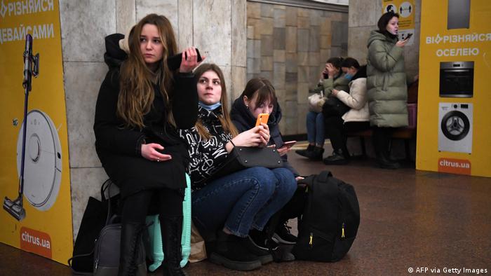 Young women hold their smartphones and look worried as they take refuge in a metro station in Kyiv in the morning of February 24, 2022