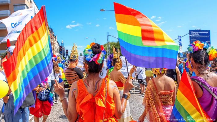 Colorfully dressed revelers brandishing rainbow flags are seen from behind at a Stockholm parade