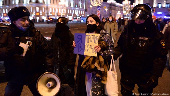 A woman holding a sign in Russian against the war in Ukraine is detained by police